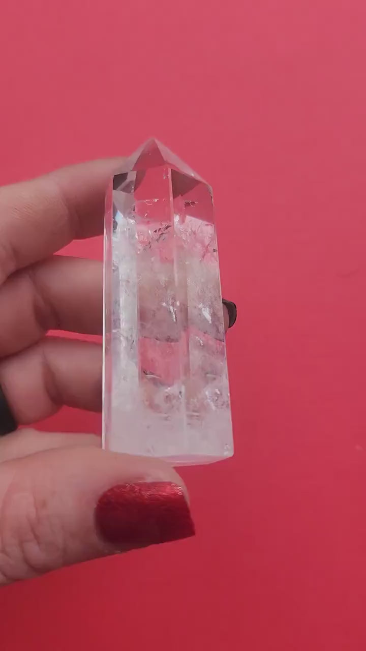 Close-up video of a polished Clear Quartz tower held in hand against a red background, showcasing natural clear quartz clarity and crystal structure, high-vibration healing crystal point for energy amplification, meditation, spiritual growth, chakra balancing, manifestation, Reiki, home altar décor, and metaphysical crystal collection