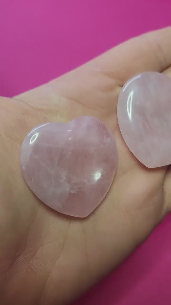 Video of me holding two Rose Quartz heart-shaped worry stones in my hand, showing their soft pink colour and smooth finish against a pink background, calming love crystal for anxiety relief and daily comfort.