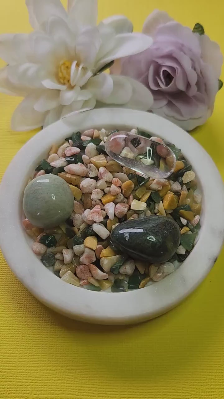 Abundance Spell Crystal Confetti Mix featuring Yellow Aventurine, Sunstone, Green Aventurine, Moss Agate, Clear Quartz, and Amazonite tumbled stones, 50g crystal mix displayed on a white dish with two flower props against a vibrant yellow background, ideal for abundance rituals, wealth manifestation grids, prosperity crystal magic, and spiritual decor.