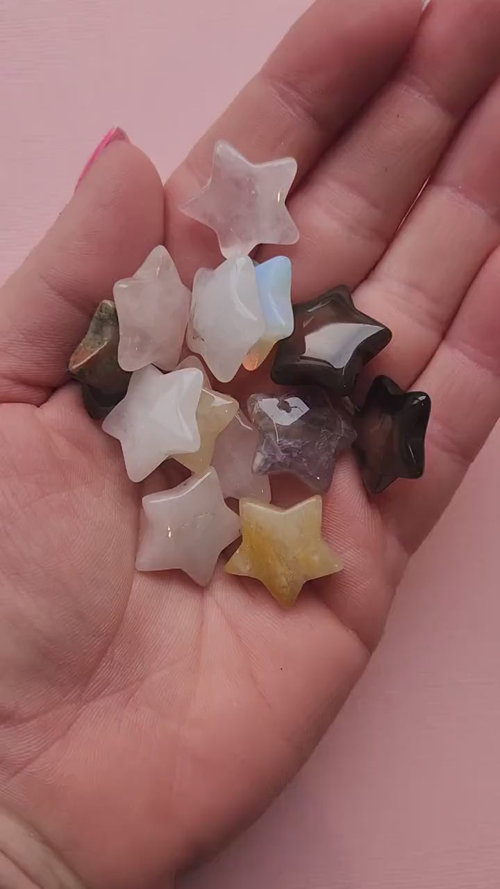 Close-up video of a hand holding an intuitively chosen mini crystal star against a light pink background. Each tiny gemstone star (approx. 2cm wide x 5mm thick) is polished from natural crystals such as Amethyst, Rose Quartz, Green Aventurine, Obsidian, and more. Perfect for altar décor, crystal grids, moon rituals, pocket talismans, manifestation work, spiritual guidance, and as a thoughtful gift for crystal lovers.