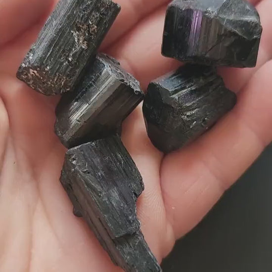 Video of hand holding raw Black Tourmaline chunks against a dark grey background. The black stones have a natural, rough texture. Perfect for protection, grounding, energy cleansing, and crystal collecting.