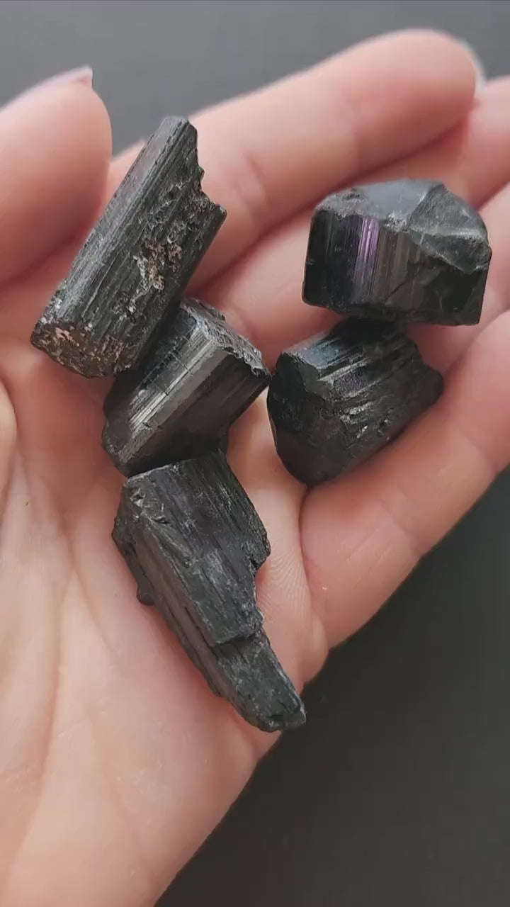 Video of hand holding raw Black Tourmaline chunks against a dark grey background. The black stones have a natural, rough texture. Perfect for protection, grounding, energy cleansing, and crystal collecting.