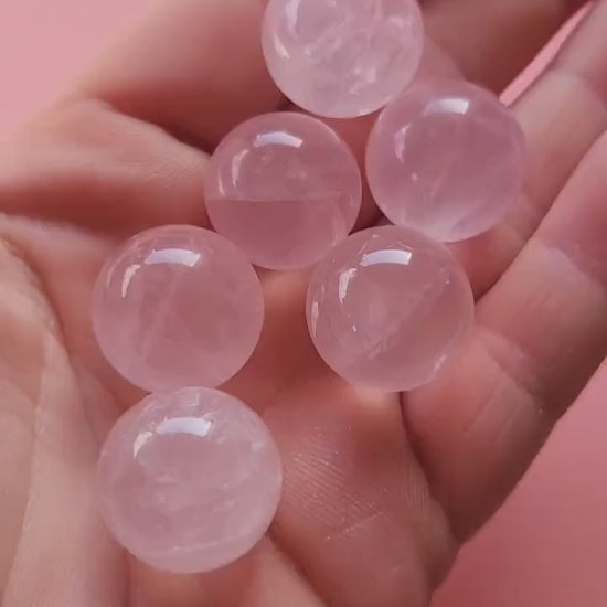 Video of a hand holding several mini rose quartz crystal spheres against a light pink background, showing their soft pink glow and polished finish. These tiny spheres radiate loving, calming energy — ideal for crystal grids, self-love rituals, and spiritual decor.