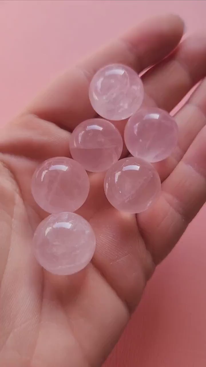 Video of a hand holding several mini rose quartz crystal spheres against a light pink background, showing their soft pink glow and polished finish. These tiny spheres radiate loving, calming energy — ideal for crystal grids, self-love rituals, and spiritual decor.