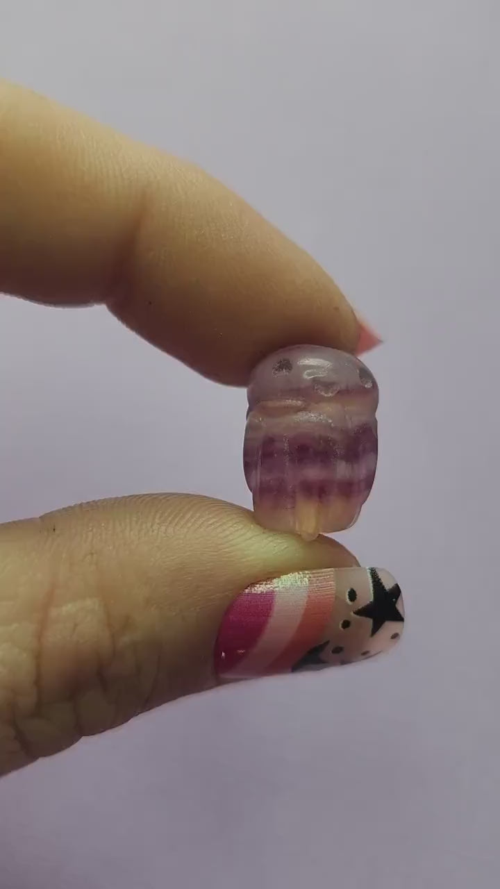 Smooth close-up video of a single fluorite mini octopus carving held between fingers, capturing the glossy polish and natural bands of purple, green and blue fluorite as it moves in the light. Clear focus on the carved tentacles and crystal details against a simple backdrop. Perfect for showcasing fluorite carvings, mini crystal animals and octopus gemstone collectibles