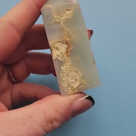 Video of Caribbean Calcite tower being held and shown off in hand against a vibrant blue backdrop, highlighting its polished orange and cream colors and smooth tower shape.