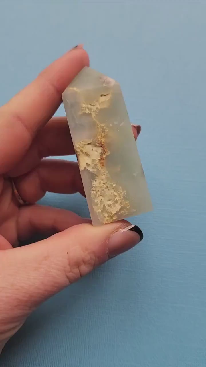 Video of Caribbean Calcite tower being held and shown off in hand against a vibrant blue backdrop, highlighting its polished orange and cream colors and smooth tower shape.