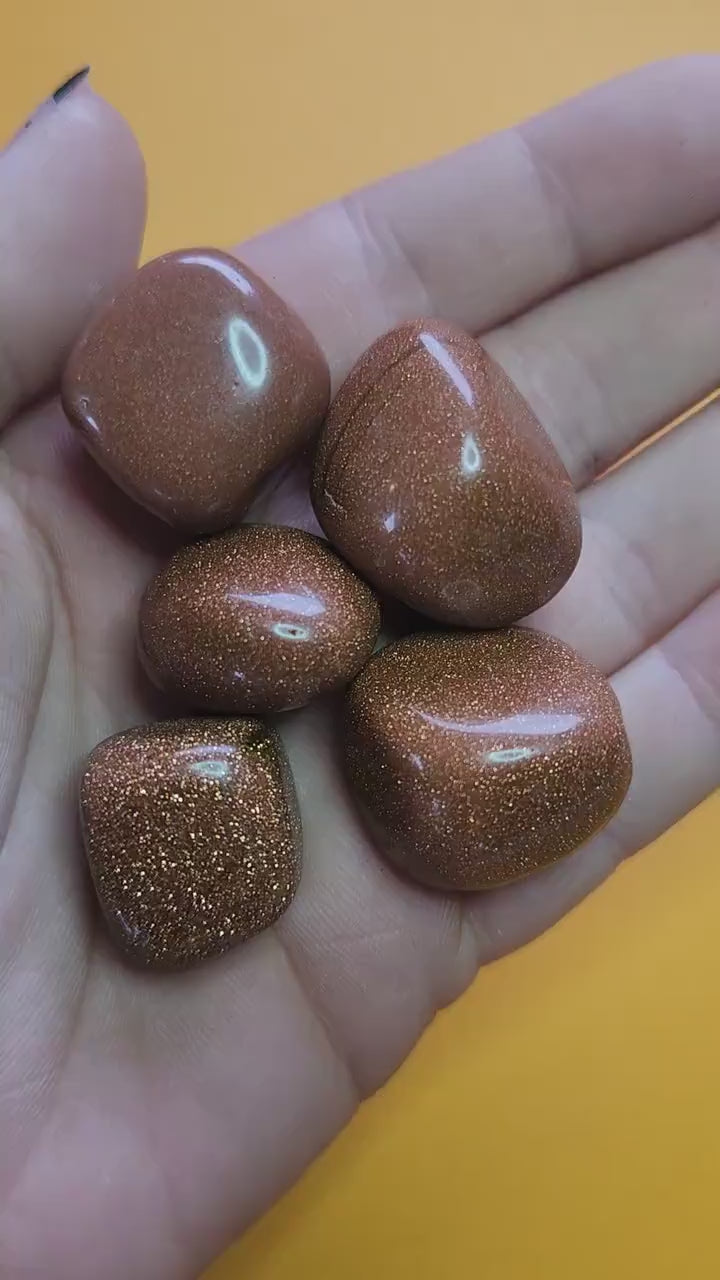Hand holding gold sandstone tumbles against a yellow background, sparkling glittery man-made goldstone crystals for confidence, motivation, and energy healing, close-up product video