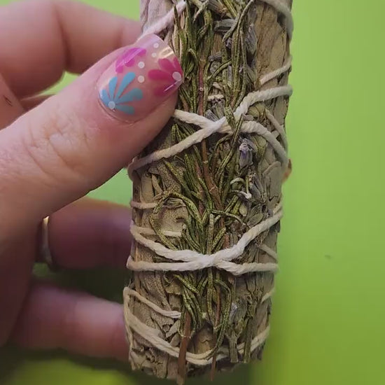 Video of a hand holding sage, lavender, and rosemary smudge sticks, highlighting their bundled herbs and natural texture — ideal for cleansing, meditation, energy clearing, and spiritual rituals.