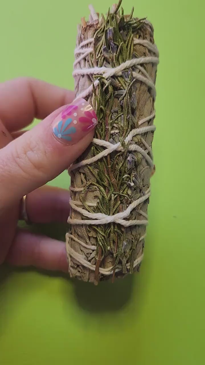Video of a hand holding sage, lavender, and rosemary smudge sticks, highlighting their bundled herbs and natural texture — ideal for cleansing, meditation, energy clearing, and spiritual rituals.