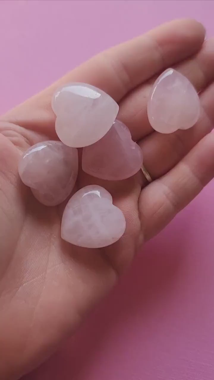 Video of a hand holding and turning a polished rose quartz heart carving against a light pink backdrop, showing its soft pink hue and smooth finish. Gentle lighting highlights the crystal’s natural shine and loving energy. Perfect for crystal healing, self-love rituals, and spiritual decor.