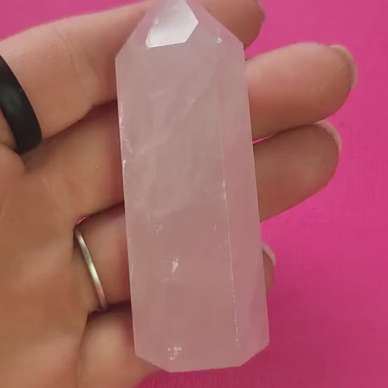 Video of a hand holding and turning a polished rose quartz crystal tower against a bright pink background, showing its soft pink hue and glossy finish. The gentle lighting highlights the stone’s natural beauty and soothing, heart-healing energy — perfect for self-love and emotional balance.