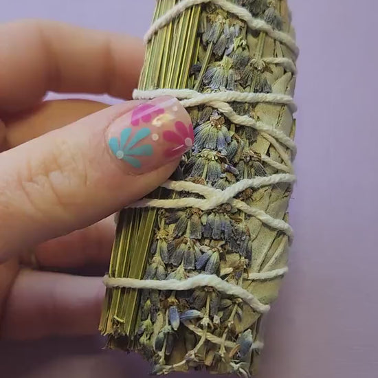 Video of a hand holding lavender and sage smudge sticks, showing their dried herbs and natural texture — perfect for cleansing, meditation, relaxation, and spiritual rituals.