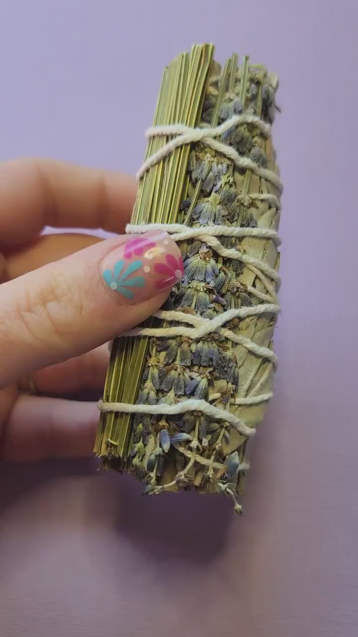 Video of a hand holding lavender and sage smudge sticks, showing their dried herbs and natural texture — perfect for cleansing, meditation, relaxation, and spiritual rituals.