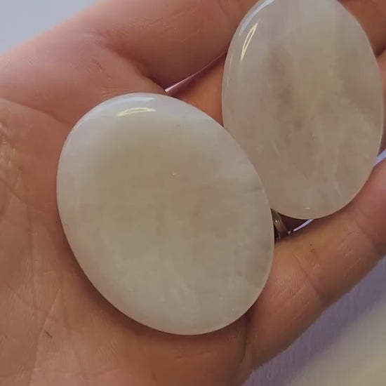 Polished Clear Quartz worry stone held in hand against a light blue background, showcasing smooth thumb-friendly shape. Master healer crystal for stress relief, meditation, manifestation, and chakra balancing.