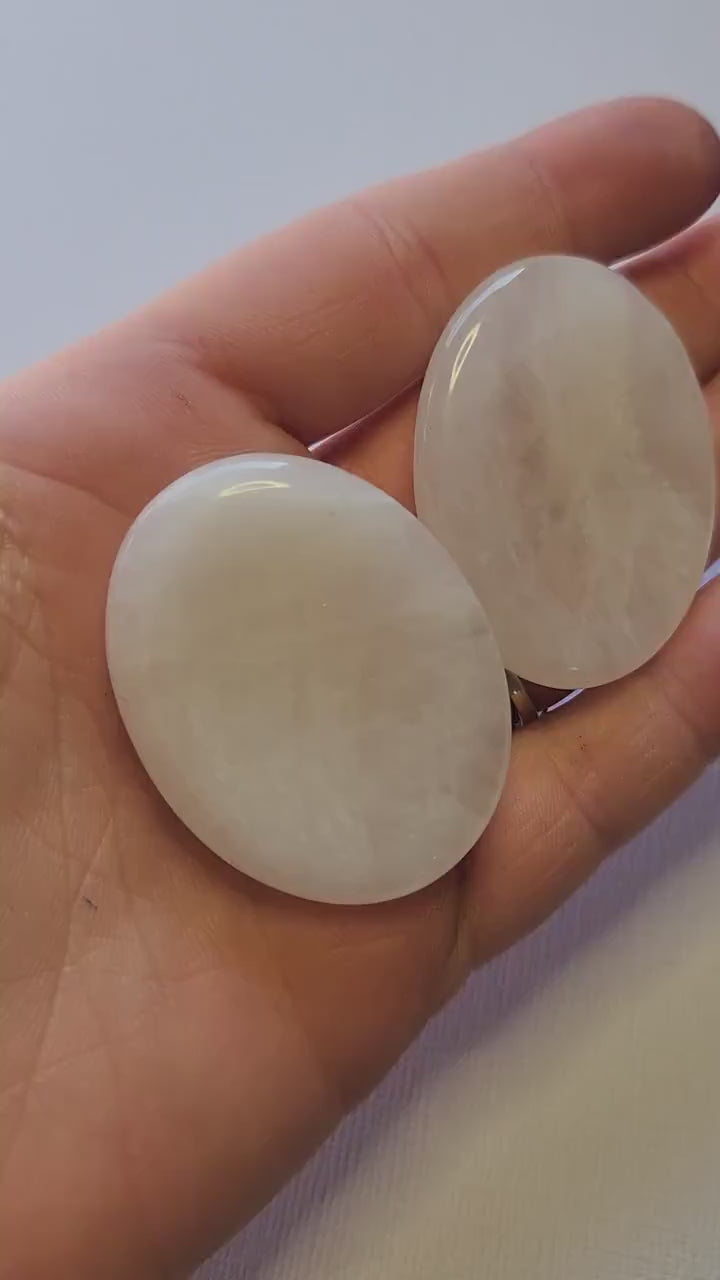 Polished Clear Quartz worry stone held in hand against a light blue background, showcasing smooth thumb-friendly shape. Master healer crystal for stress relief, meditation, manifestation, and chakra balancing.
