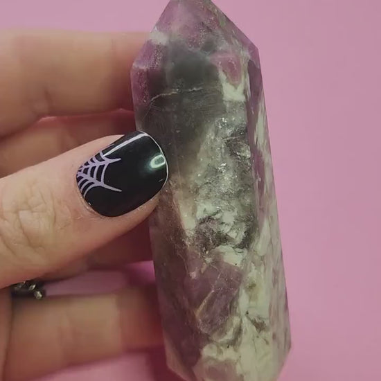 Video of a pink tourmaline crystal tower being held up in hand against a pink background, showing polished gemstone point, natural pink veining, high-quality healing crystal for heart chakra energy, emotional healing, spiritual cleansing and crystal collection display.