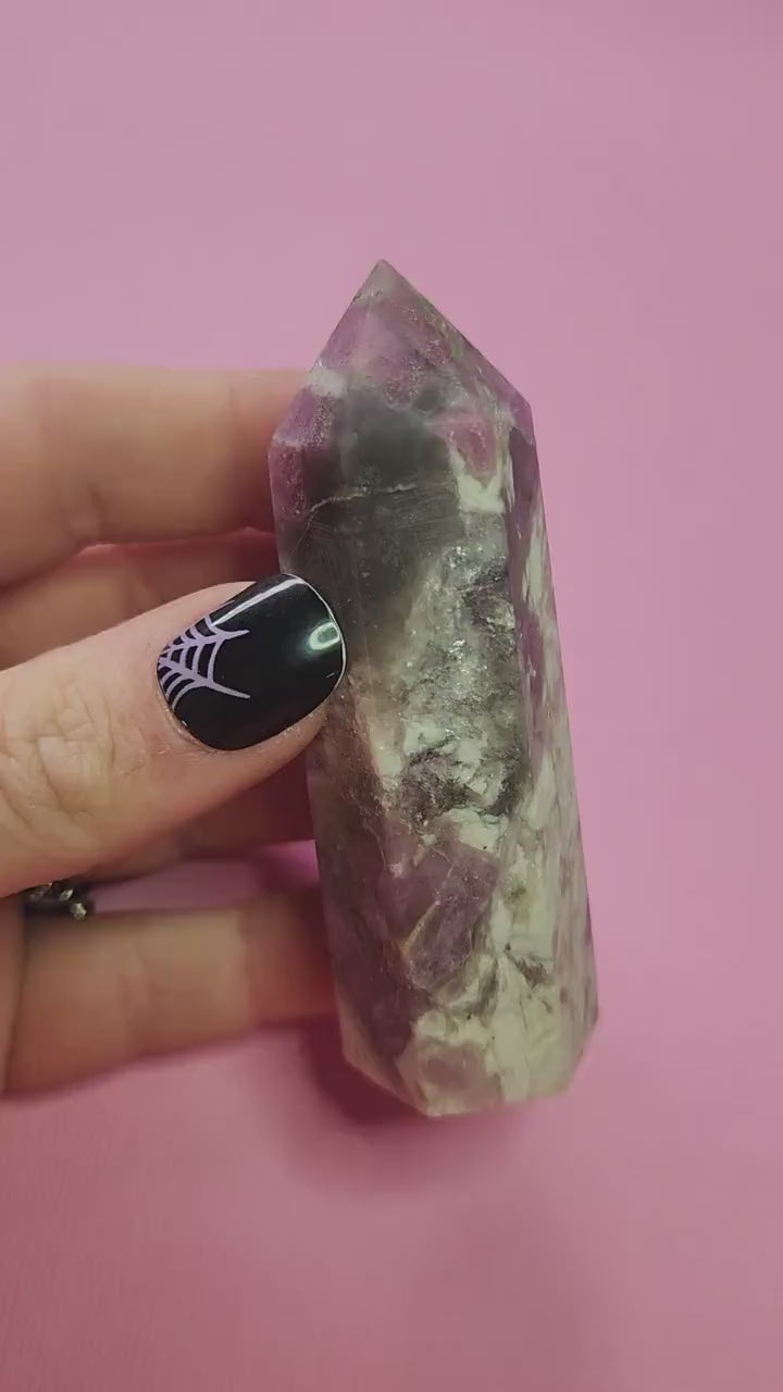 Video of a pink tourmaline crystal tower being held up in hand against a pink background, showing polished gemstone point, natural pink veining, high-quality healing crystal for heart chakra energy, emotional healing, spiritual cleansing and crystal collection display.