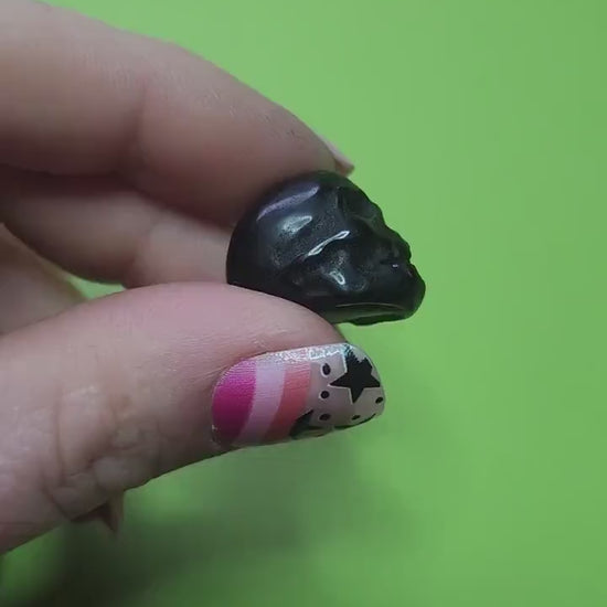 Close-up video of a hand holding a mini Black Obsidian crystal skull with a vibrant green background, showcasing polished surface and detailed carving. Perfect for protection, shadow work, Halloween decor, and carved crystal skull collectors.