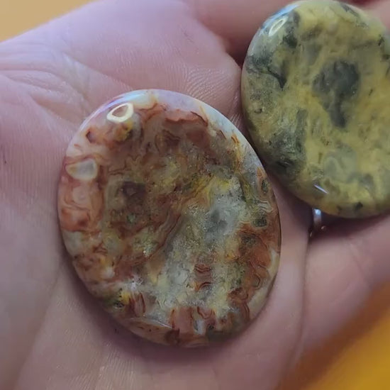 Video of a hand holding several polished Crazy Lace Agate worry stones up close against a yellow background, showcasing their smooth, tactile surface, intricate banded patterns, and natural colors — perfect for stress relief, grounding, and crystal healing.