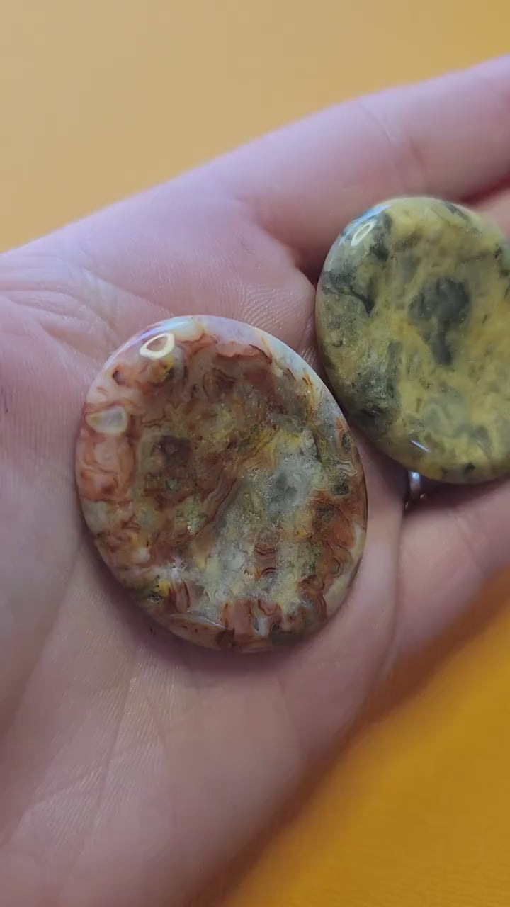 Video of a hand holding several polished Crazy Lace Agate worry stones up close against a yellow background, showcasing their smooth, tactile surface, intricate banded patterns, and natural colors — perfect for stress relief, grounding, and crystal healing.