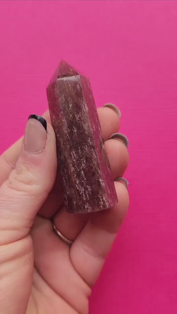 Close-up video of a polished Strawberry Quartz tower held in hand against a pink background, showcasing the pink crystal clarity, sparkly inclusions, and natural gemstone texture; high-vibration healing crystal point for heart chakra work, self-love energy, emotional balance, and spiritual crystal lovers