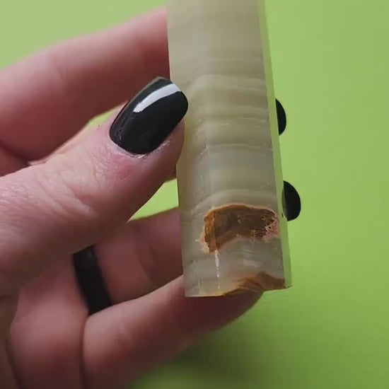 Hand holding and showcasing a polished Afghan Jade crystal tower against a bright green background, highlighting its rich green hues and natural texture.