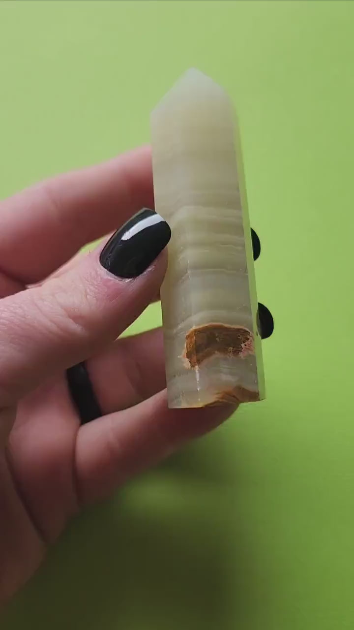 Hand holding and showcasing a polished Afghan Jade crystal tower against a bright green background, highlighting its rich green hues and natural texture.