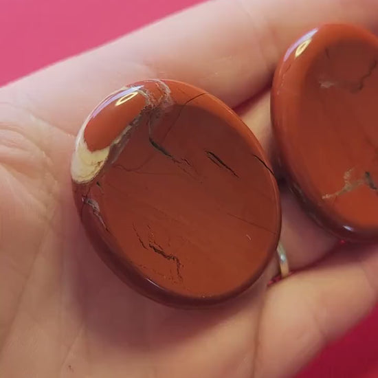 Video of a hand holding several Red Jasper worry stones, showing their deep red color, smooth polished surface, and natural variations. Perfect for grounding, meditation, Reiki, crystal healing, and spiritual energy work. Ideal for crystal collectors and stress relief.