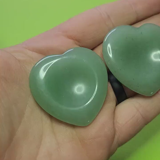 Showing two Green Aventurine heart-shaped worry stones in my hand against a green background, polished pocket crystals for luck, prosperity, stress relief, and calming energy.
