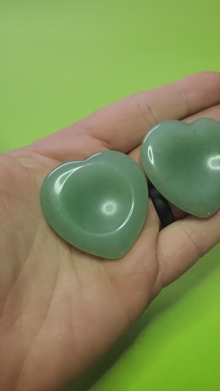 Showing two Green Aventurine heart-shaped worry stones in my hand against a green background, polished pocket crystals for luck, prosperity, stress relief, and calming energy.