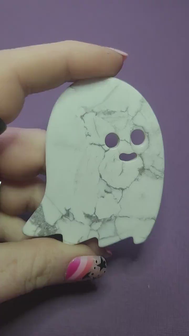 Close-up of a hand holding a carved white Howlite ghost slice with natural grey veining against a dark purple backdrop. Flat, palm-sized ghost crystal perfect for Halloween altars, witchy décor, crystal grids, meditation, calming energy, spiritual practice, and spooky-season gifts.