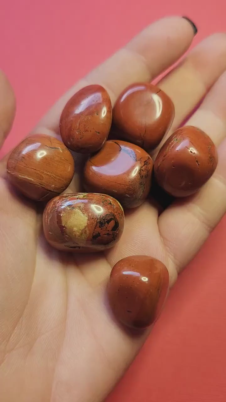 Video of a hand holding polished Red Jasper tumbles against a red background, highlighting their deep red color and smooth finish — ideal for grounding, stability, and crystal healing.