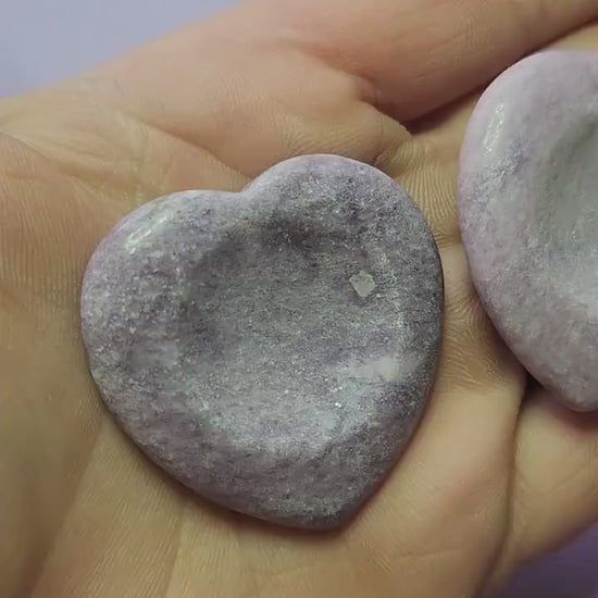 Showing two Lepidolite heart worry stones in hand on a lavender background, polished semi-precious crystals for stress relief, meditation, anxiety support, and spiritual healing.