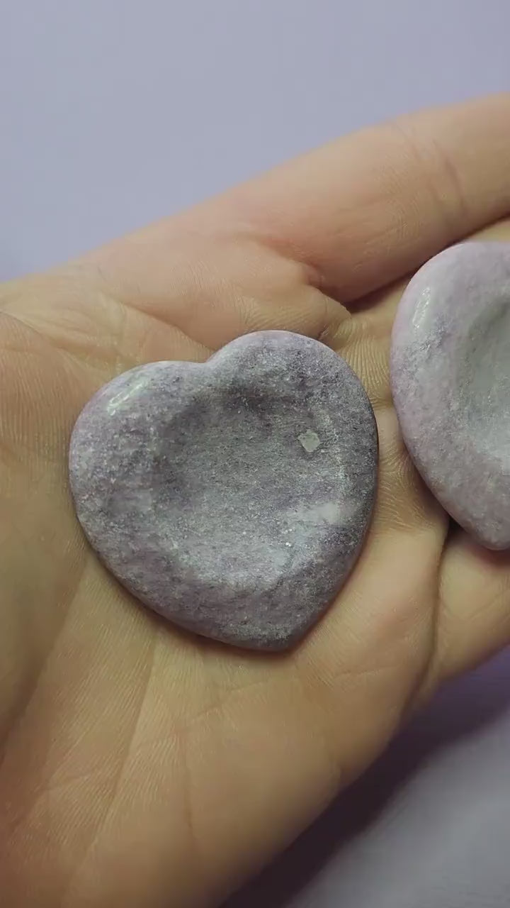 Showing two Lepidolite heart worry stones in hand on a lavender background, polished semi-precious crystals for stress relief, meditation, anxiety support, and spiritual healing.