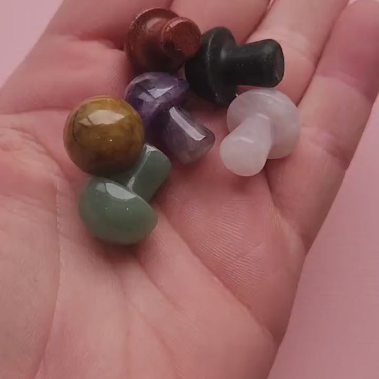 Close-up video of assorted mini mystery crystal mushrooms displayed against a light pink background. Each tiny gemstone carving is approximately 2cm tall, polished from natural crystals such as Amethyst, Rose Quartz, Fluorite, and more. Intuitively chosen crystals symbolizing growth, grounding, and transformation. Perfect for witchy décor, altar setups, crystal collections, or as thoughtful gifts for spiritual practitioners.