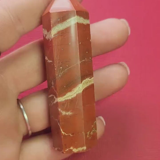Video of a hand holding a polished Red Jasper crystal tower up close against a red background, highlighting its deep red color, natural striations, and smooth polished finish. Perfect for crystal healing, grounding, energy work, meditation, Reiki, and spiritual decor. Ideal for crystal collectors, home altars, and intention setting.
