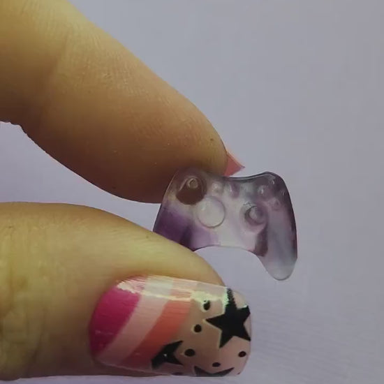 Close-up video of a single fluorite mini game controller carving held in hand, showing polished details and natural purple, green and blue fluorite banding as it catches the light against a lavender backdrop. Perfect for fluorite carvings, gamer-themed crystal collectibles and unique gemstone gifts