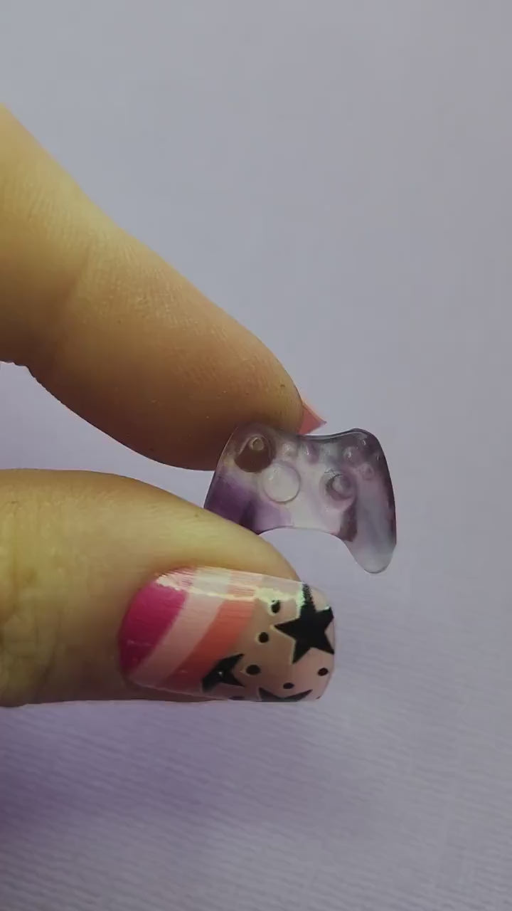 Close-up video of a single fluorite mini game controller carving held in hand, showing polished details and natural purple, green and blue fluorite banding as it catches the light against a lavender backdrop. Perfect for fluorite carvings, gamer-themed crystal collectibles and unique gemstone gifts