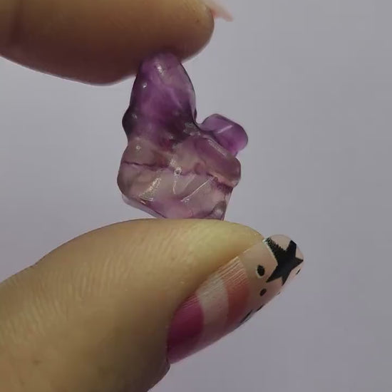 Close-up video of a single fluorite mini fairy carving held in hand, showing polished details and natural purple, green and blue fluorite banding as it catches the light against a lavender backdrop. Ideal for fluorite carvings, mini crystal fairies and collectible gemstone figures