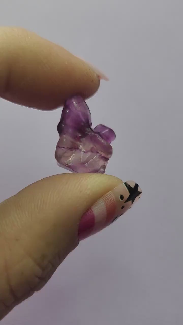 Close-up video of a single fluorite mini fairy carving held in hand, showing polished details and natural purple, green and blue fluorite banding as it catches the light against a lavender backdrop. Ideal for fluorite carvings, mini crystal fairies and collectible gemstone figures