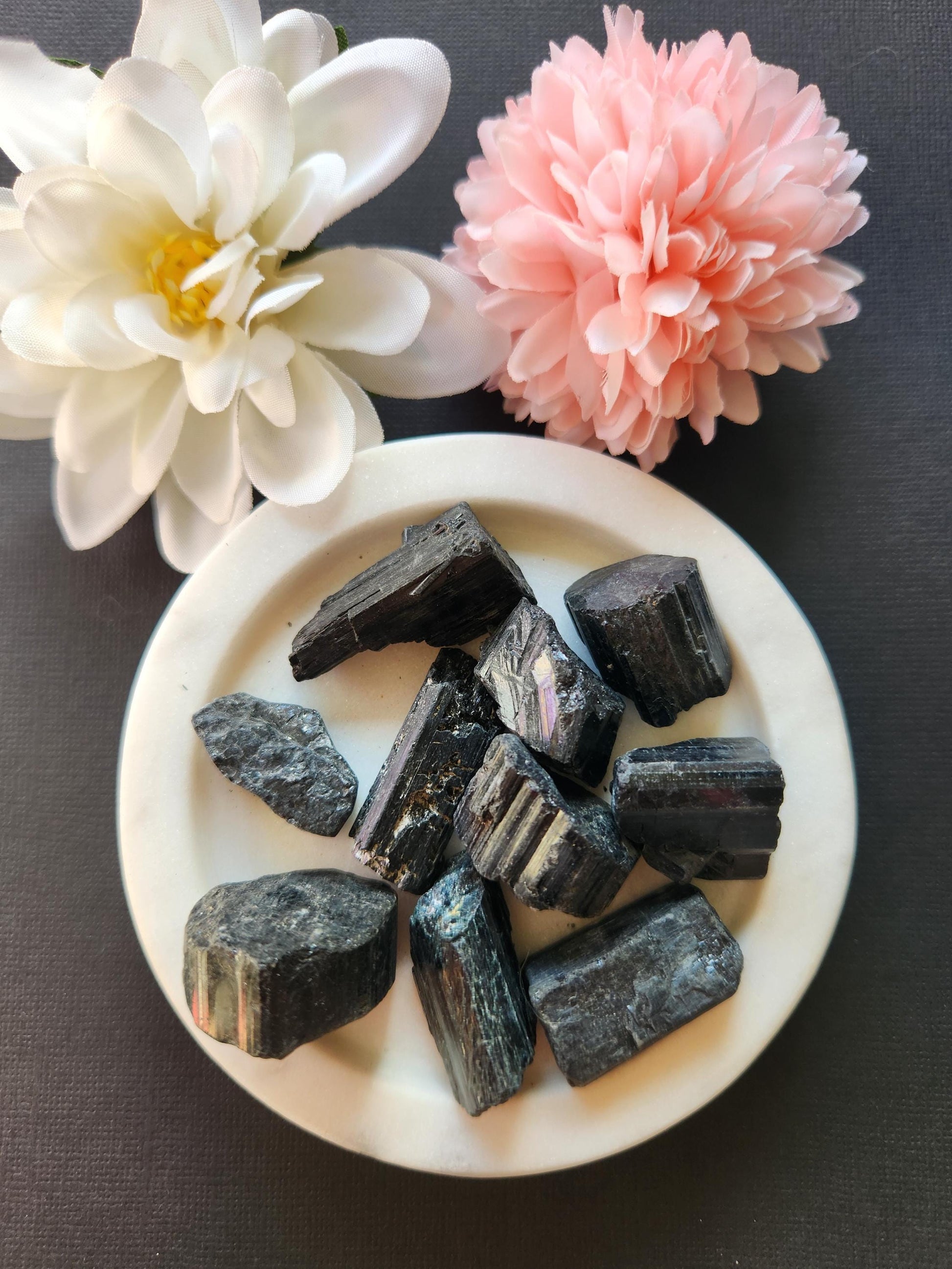 Raw Black Tourmaline crystal displayed on a black background, showcasing its natural, rugged texture and deep black color. Known for its powerful grounding and protective properties, this unpolished stone is ideal for EMF shielding, spiritual healing, and balancing the Root Chakra. The dark backdrop emphasizes the crystal’s natural striations and rough edges, making it perfect for collectors, healers, and witchcraft supplies.