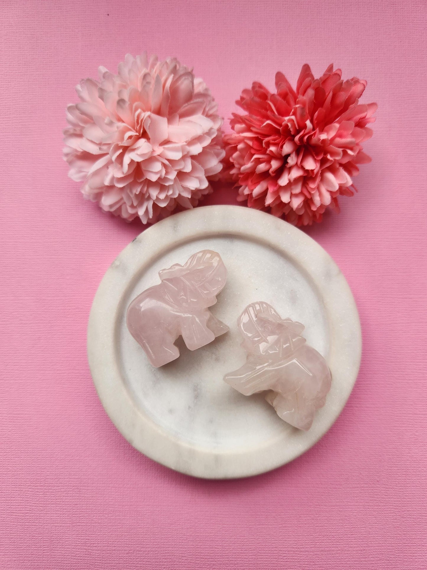 Rose quartz elephant crystal carving displayed in a white dish with floral props on a soft pink background, polished gemstone animal figurine for crystal decor and gifting