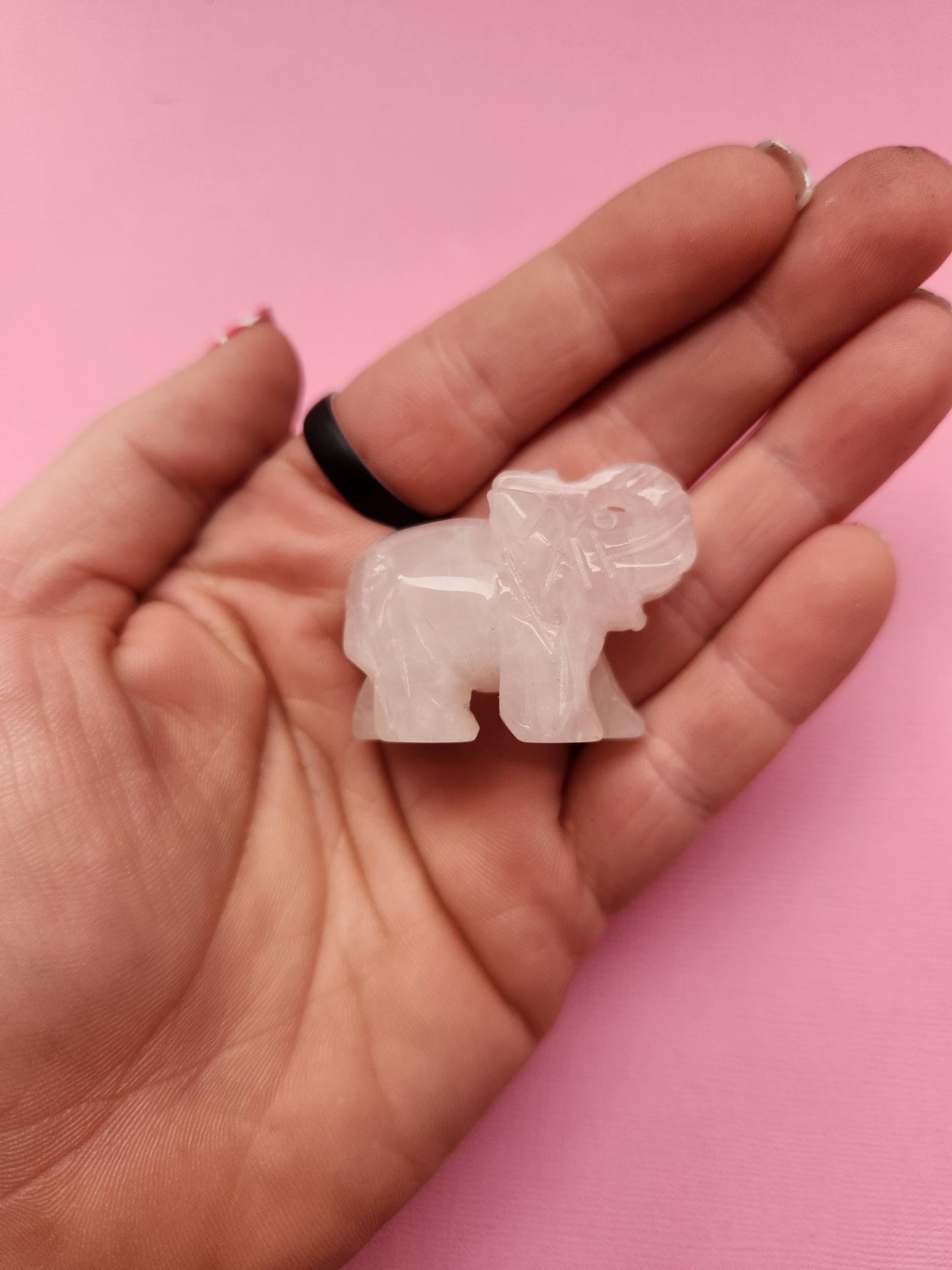 Rose quartz elephant crystal carving held in hand against a pink background, polished gemstone animal figurine showcasing size and detail for crystal collectors and gifts