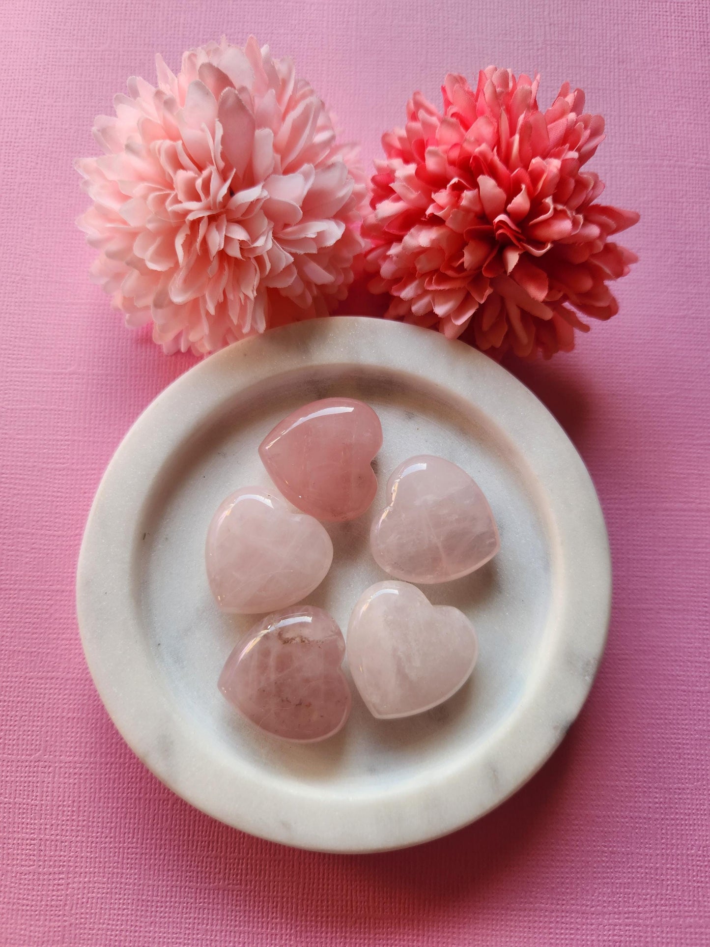 Rose Quartz hearts displayed on a soft pink background, highlighting their gentle pink tones and smooth, polished surfaces. These heart-shaped crystals are known for promoting self-love, emotional healing, and heart chakra balance. The monochromatic pink backdrop enhances the soothing and romantic energy of the stones, making them ideal for gifting, spiritual practices, or crystal healing collections.
