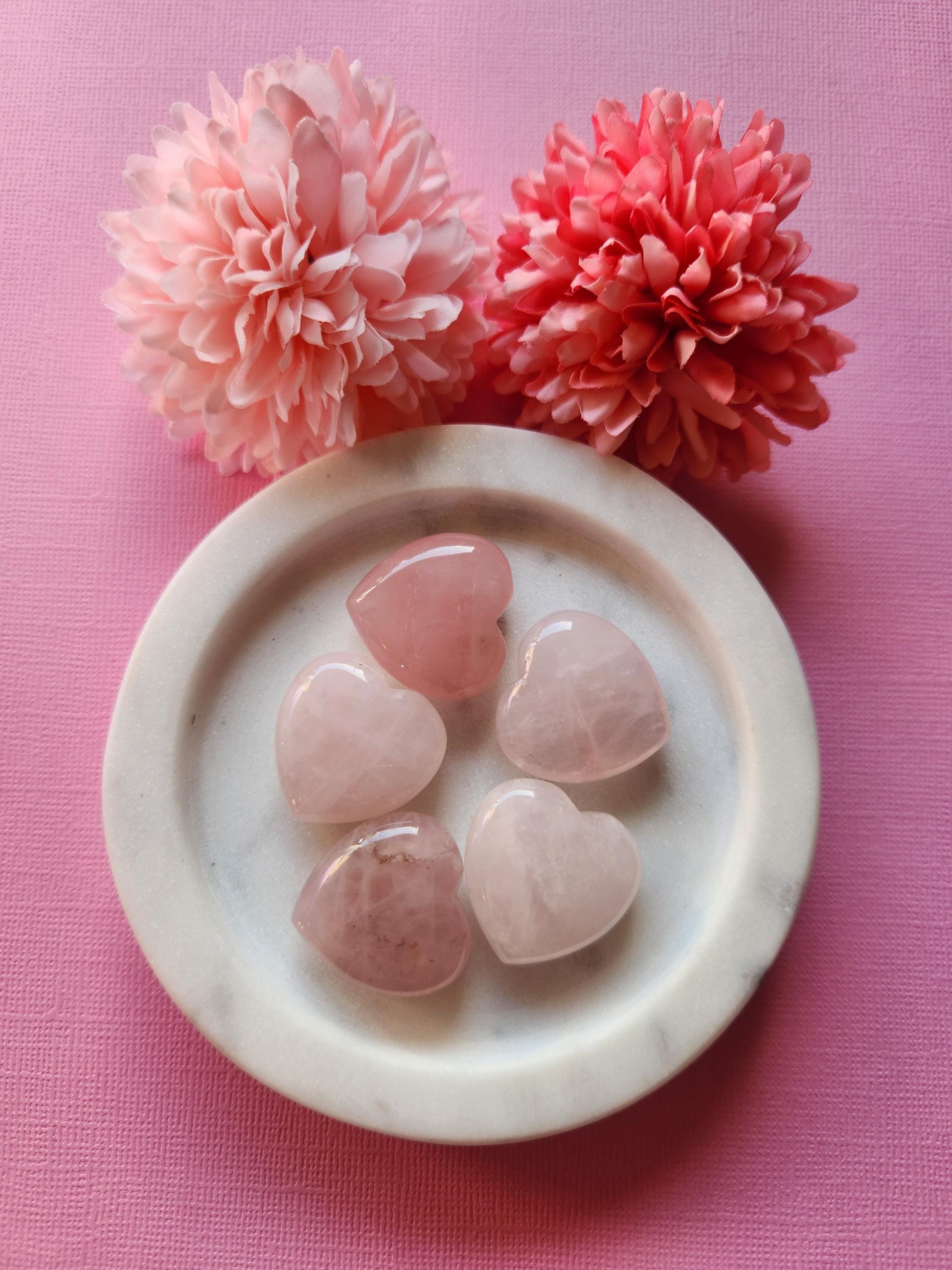 Rose Quartz hearts displayed on a soft pink background, highlighting their gentle pink tones and smooth, polished surfaces. These heart-shaped crystals are known for promoting self-love, emotional healing, and heart chakra balance. The monochromatic pink backdrop enhances the soothing and romantic energy of the stones, making them ideal for gifting, spiritual practices, or crystal healing collections.