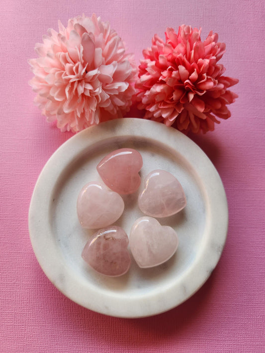 Rose Quartz hearts displayed on a soft pink background, highlighting their gentle pink tones and smooth, polished surfaces. These heart-shaped crystals are known for promoting self-love, emotional healing, and heart chakra balance. The monochromatic pink backdrop enhances the soothing and romantic energy of the stones, making them ideal for gifting, spiritual practices, or crystal healing collections.