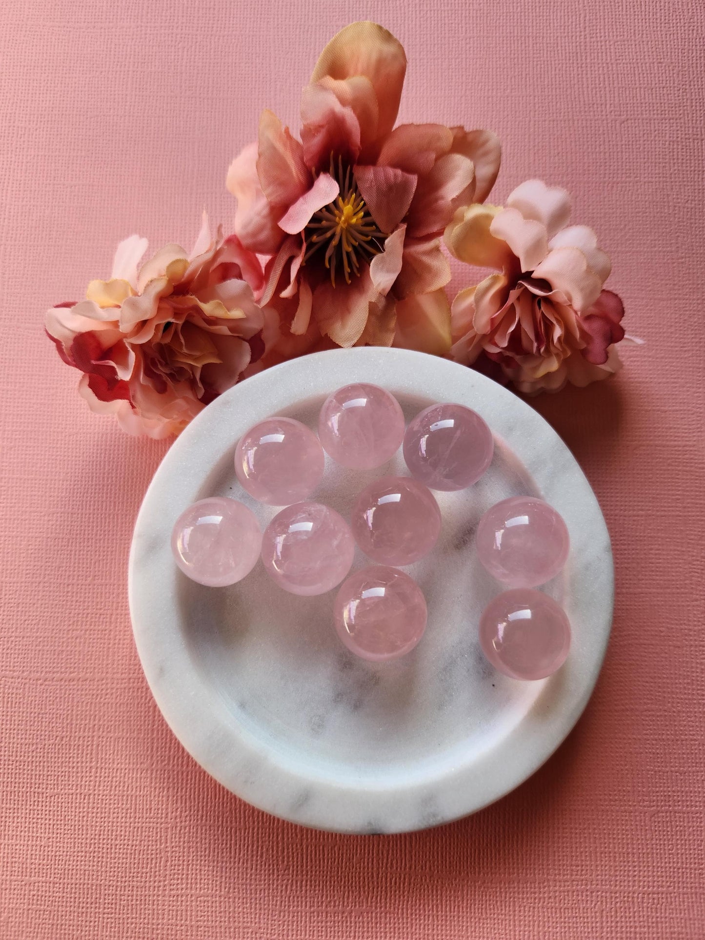 Rose Quartz mini spheres displayed on a soft pink background, showcasing their smooth polished surfaces and gentle pink tones. These small crystal balls are known for promoting love, emotional healing, and heart chakra balance. The pink backdrop enhances the warm, soothing energy of the rose quartz, making them perfect for meditation, self-love rituals, gifting, or crystal collections.