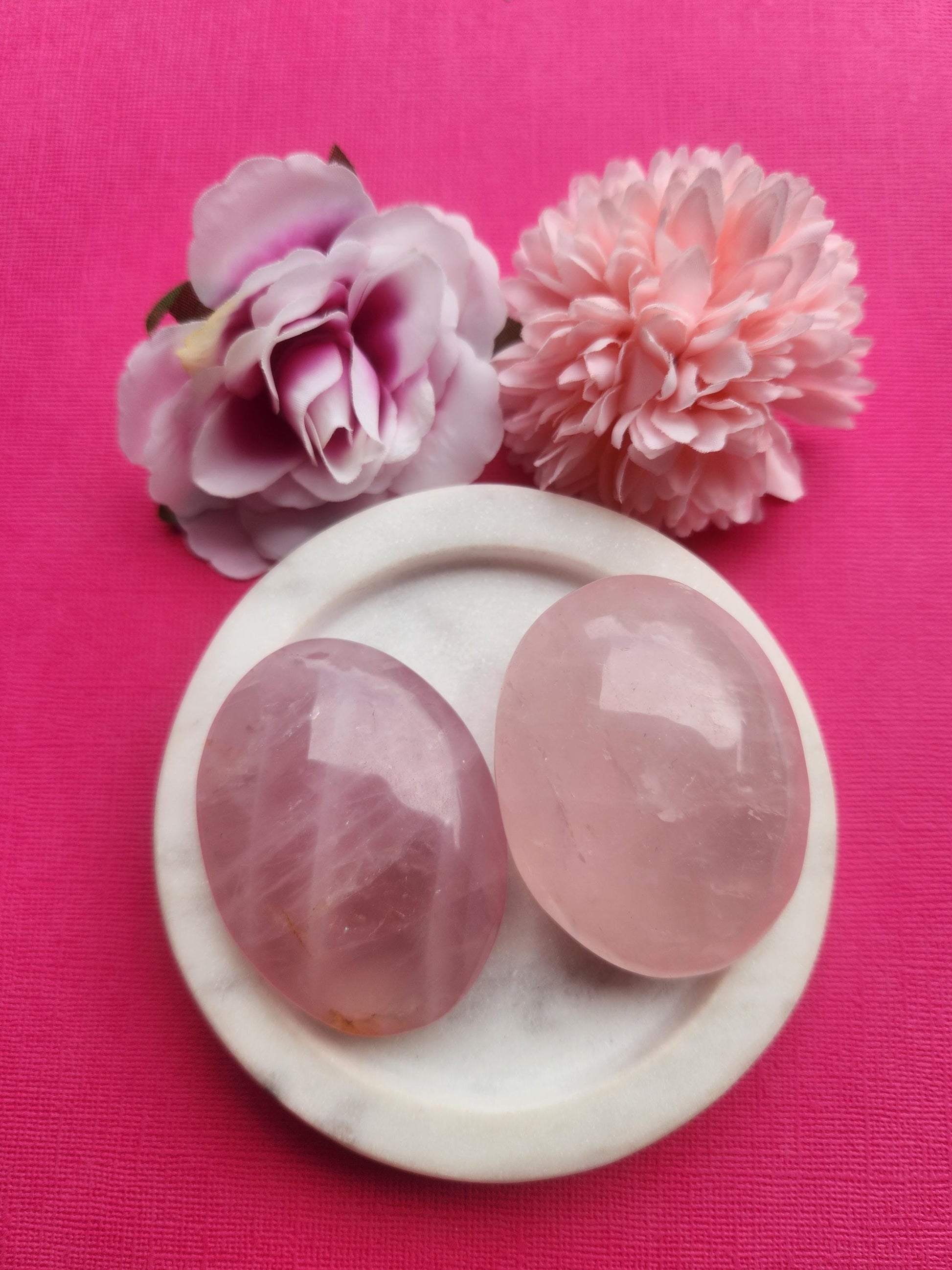 Rose quartz palmstone displayed in a white ceramic dish with two floral props on a soft pink background, featuring polished natural rose quartz crystal, healing gemstone palm stone for love self love and emotional healing energy, metaphysical crystal perfect for gifting meditation altar decor and crystal collections