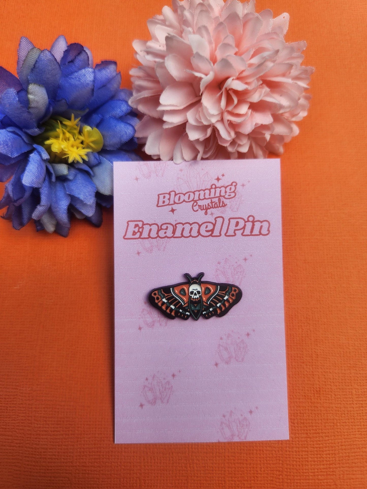Skull moth enamel pin featuring orange and blue moth with skull on its back, gothic insect inspired design, dark aesthetic witchy enamel pin, occult nature themed lapel badge, mystical horror style pin for bags jackets hats and enamel pin collections